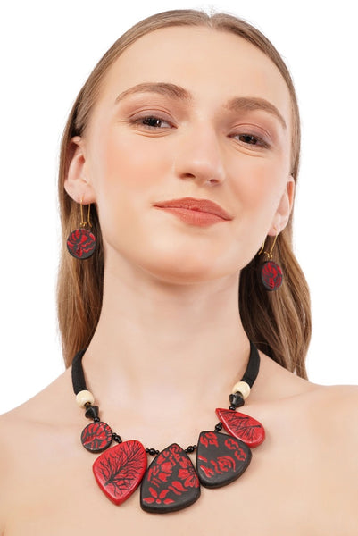 Woman wearing a red and black floral necklace and earrings on a white background