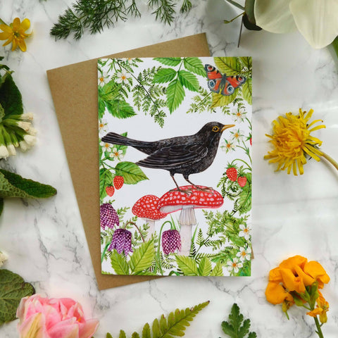 Greeting card with a bird design surrounded by flowers and leaves on a marble surface