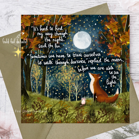 Greeting card with fox and moon illustration and inspirational quote on a wooden surface.