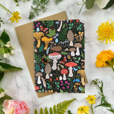 Greeting card with mushroom design surrounded by flowers and leaves on a marble surface
