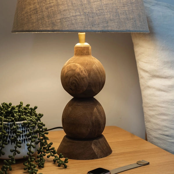 Wooden lamp with a textured shade on a table next to a plant and a watch.