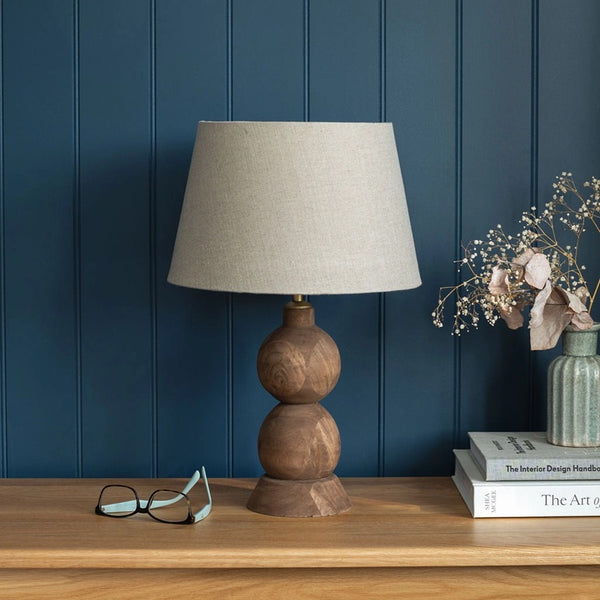 Wooden lamp with beige shade on a wooden table against a blue paneled wall.