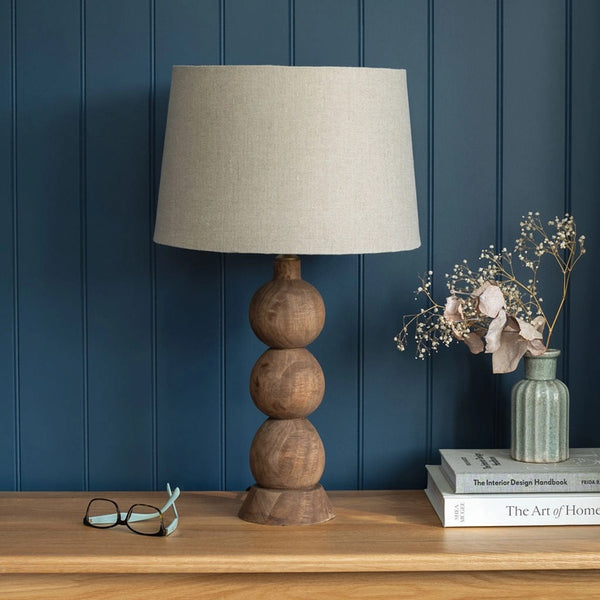 Table lamp with a beige shade on a wooden surface against a blue paneled wall.