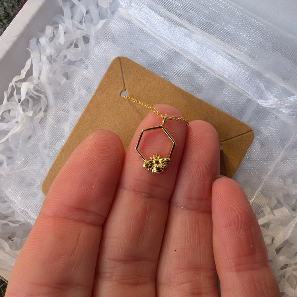 Gold necklace with a hexagonal pendant held between fingers against a white textured background