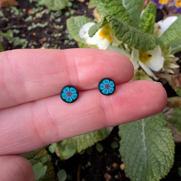 Blue floral earrings held between fingers with a natural background