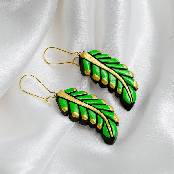 Green leaf-shaped earrings with gold accents on a white fabric background