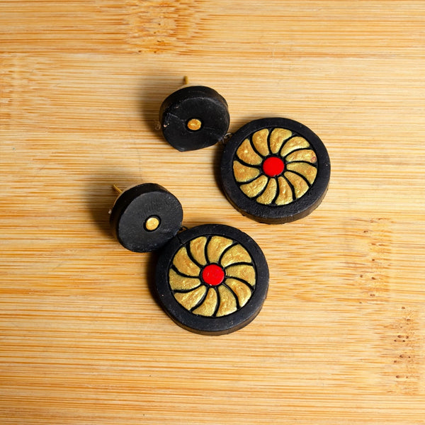 Three circular objects with black outer rims, gold inner patterns, and red centers on a wooden surface.