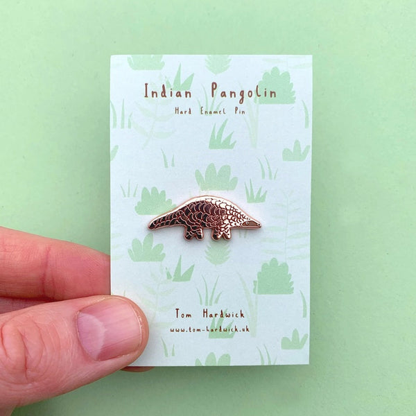 Indian Pangolin enamel pin on a card held by a hand with a green background