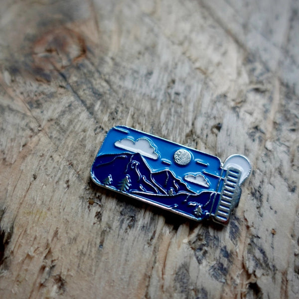 Enamel pin with mountain and moon design on a wooden surface