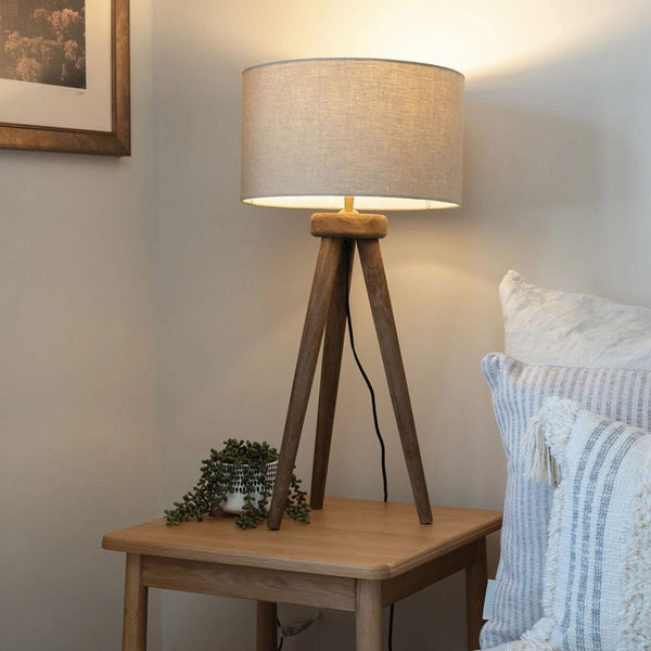 Wooden table lamp with a beige shade on a wooden side table in a bedroom setting.