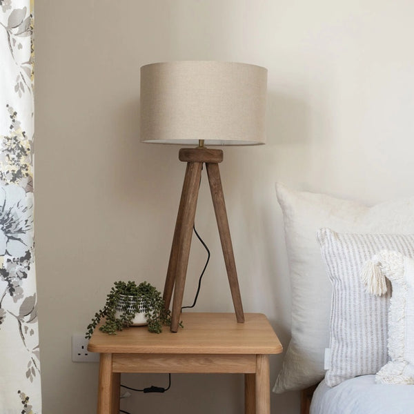 Wooden side table with a tripod lamp and small plant in a bedroom setting.