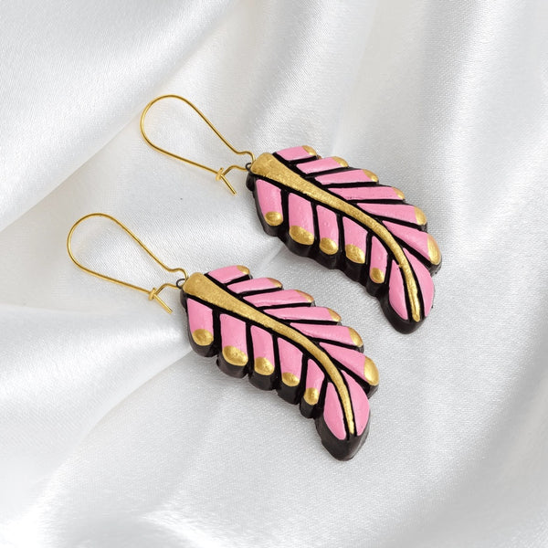 Pink and gold feather-shaped earrings on a white fabric background