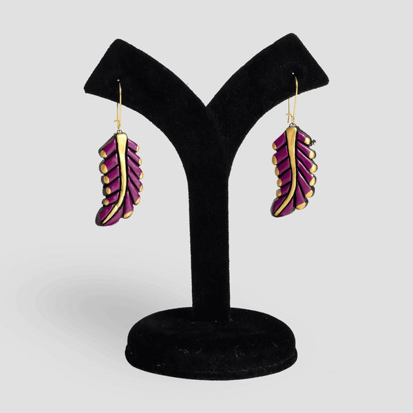 Purple feather-shaped earrings on a black velvet stand against a white background
