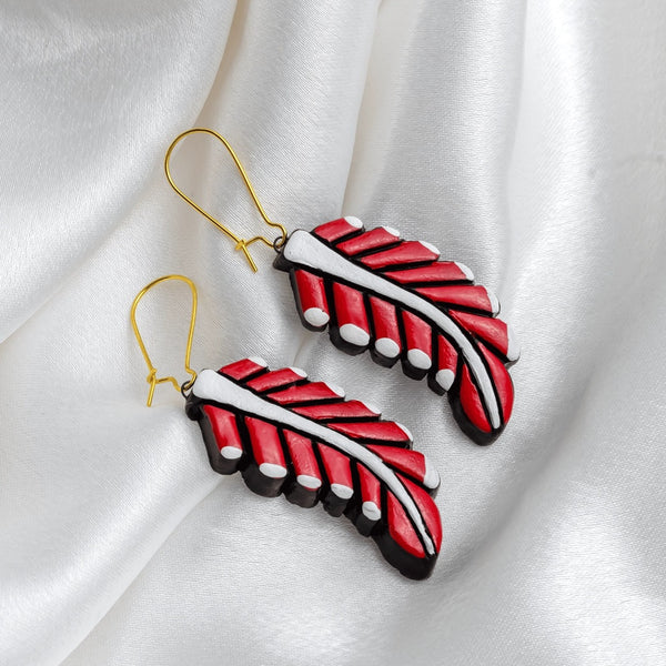 Red and black feather-shaped earrings on a white fabric background