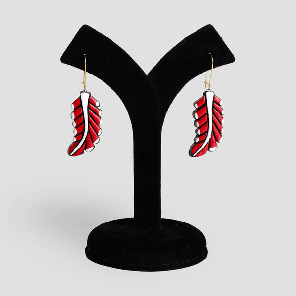 Red feather-shaped earrings on a black stand against a light gray background