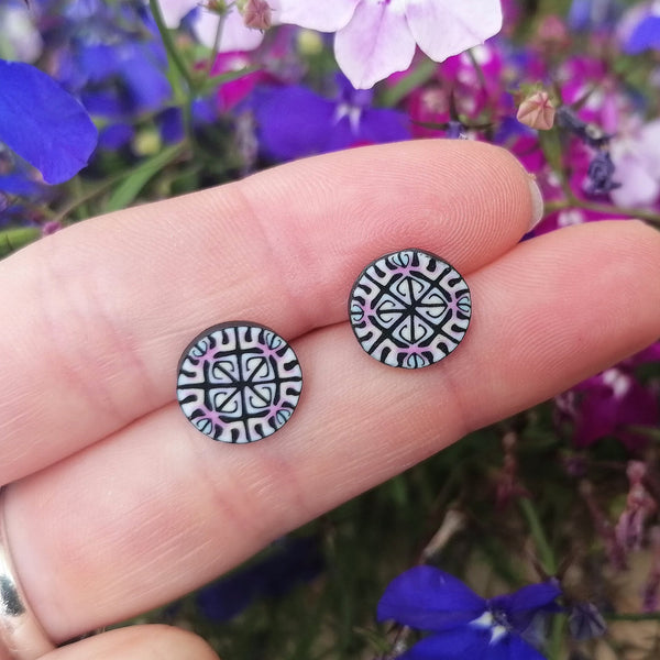 Round black and white patterned earrings held between fingers with a blurred floral background