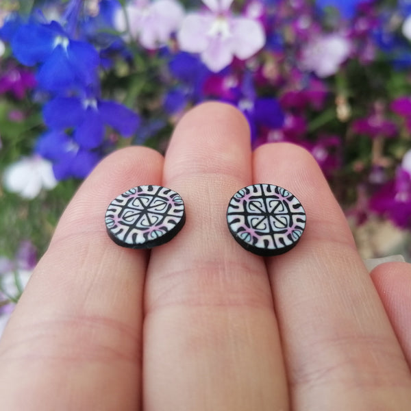 Round black and white patterned earrings held between fingers with a floral background