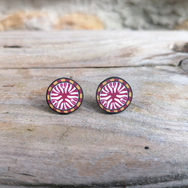 Pair of round earrings with pink and black design on a wooden surface