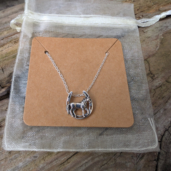 Silver necklace with a horse design on a brown card, placed on a wooden surface.