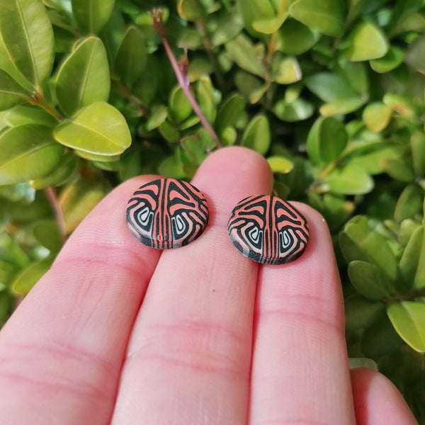 Pair of earrings with a tribal design held between fingers against a green leafy background