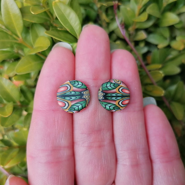 Pair of decorative earrings held between fingers with a green leafy background