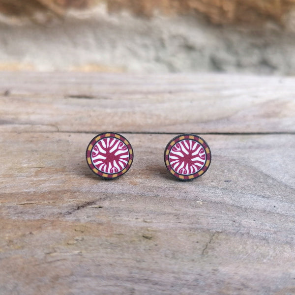 Round earrings with a pink and gold design on a wooden surface