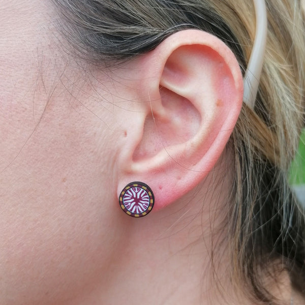 Close-up of an ear with a circular earring featuring a design.
