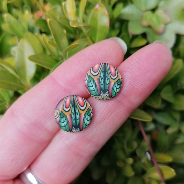 Colorful patterned earrings held between fingers against a green leafy background