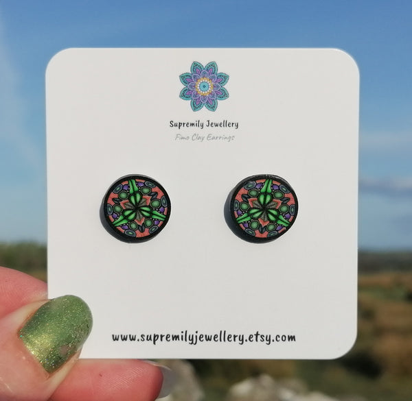 Pair of round earrings with a floral design on a Supremily Jewellery card against a blurred natural background.
