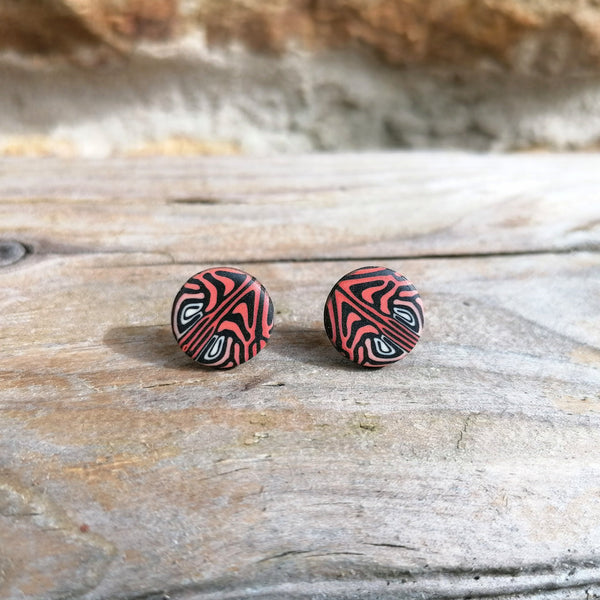 Pair of round earrings with a black and red pattern on a wooden surface