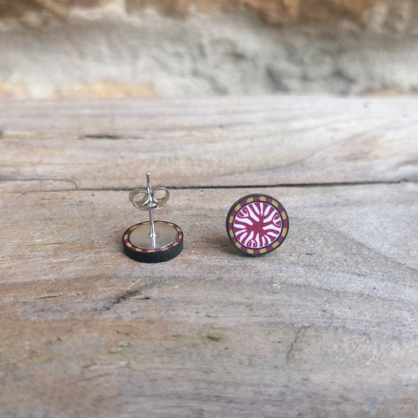Pair of round earrings with pink and black design on a wooden surface