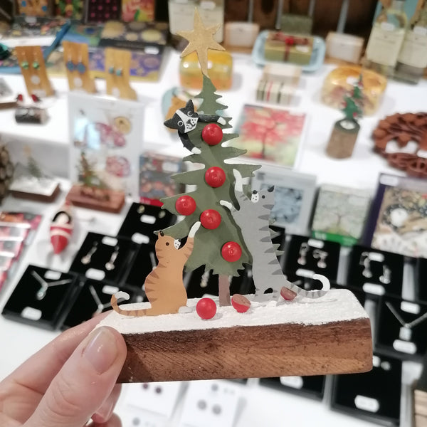 Small decorative figure of a cat and tree held in front of a store display with various items.
