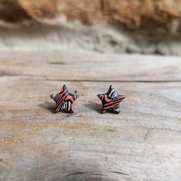 Star-shaped earrings with black and red pattern on a wooden surface