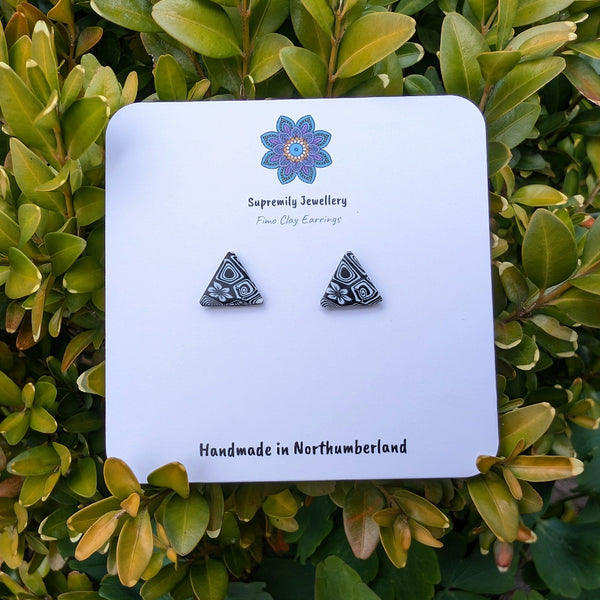 Pair of triangle-shaped earrings on a Supremely Jewellery card against a green leafy background