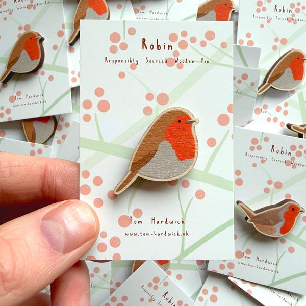 Robin brooch on a card held by a hand with more brooches and cards in the background.