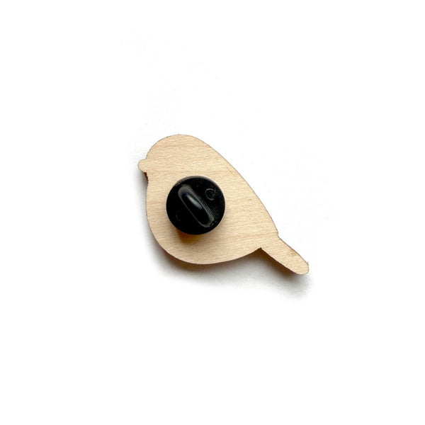 Wooden bird-shaped object with a black button on a white background