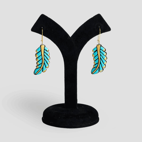 Turquoise feather-shaped earrings on a black velvet stand against a white background