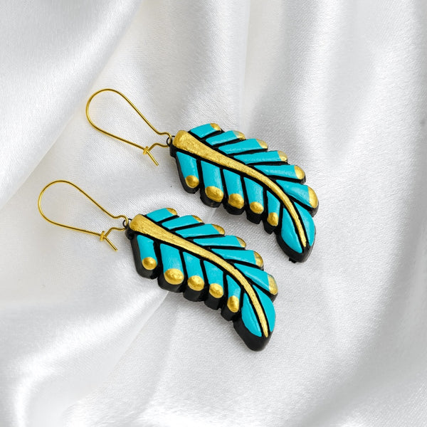 Pair of feather-shaped earrings with turquoise and gold design on a white fabric background
