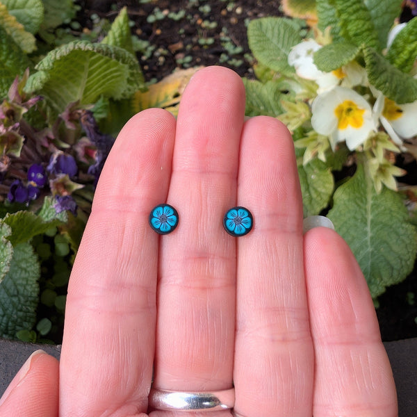 Small blue flower earrings held between fingers with a natural background