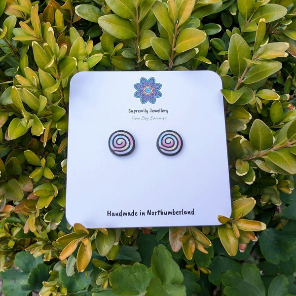 Pair of spiral patterned earrings on a Supremia Jewellery card against a green leafy background