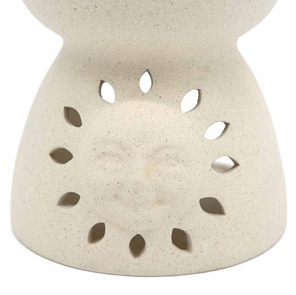 Close-up of a speckled cream ceramic diffuser or candle holder with a sun face design visible through the leaf-shaped cutouts, on a white background.
