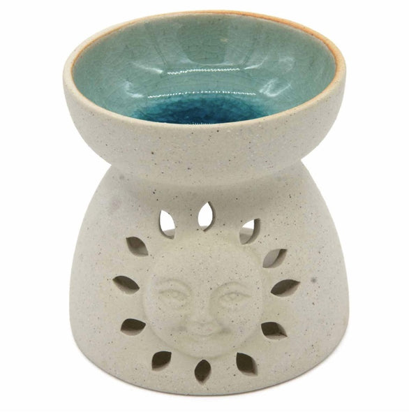 A ceramic oil burner holder with a speckled light beige exterior, featuring a sun face cutout on the front and a glazed teal-blue interior, shown on a white background.